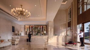 A spacious lobby with a chandelier, a reception desk, a plush sofa, and a cart. - Venus International Hotel (Foshan)