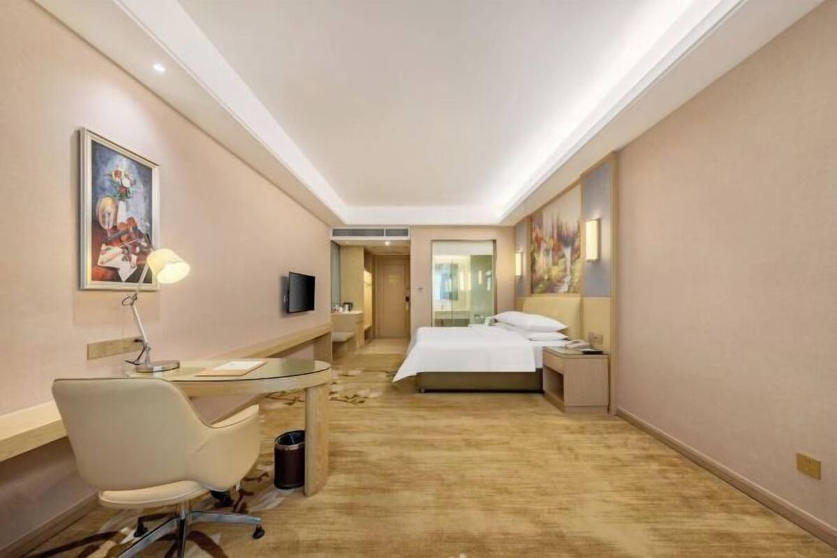 A hotel room with a bed, a desk with a chair, a television, and artwork on the walls.