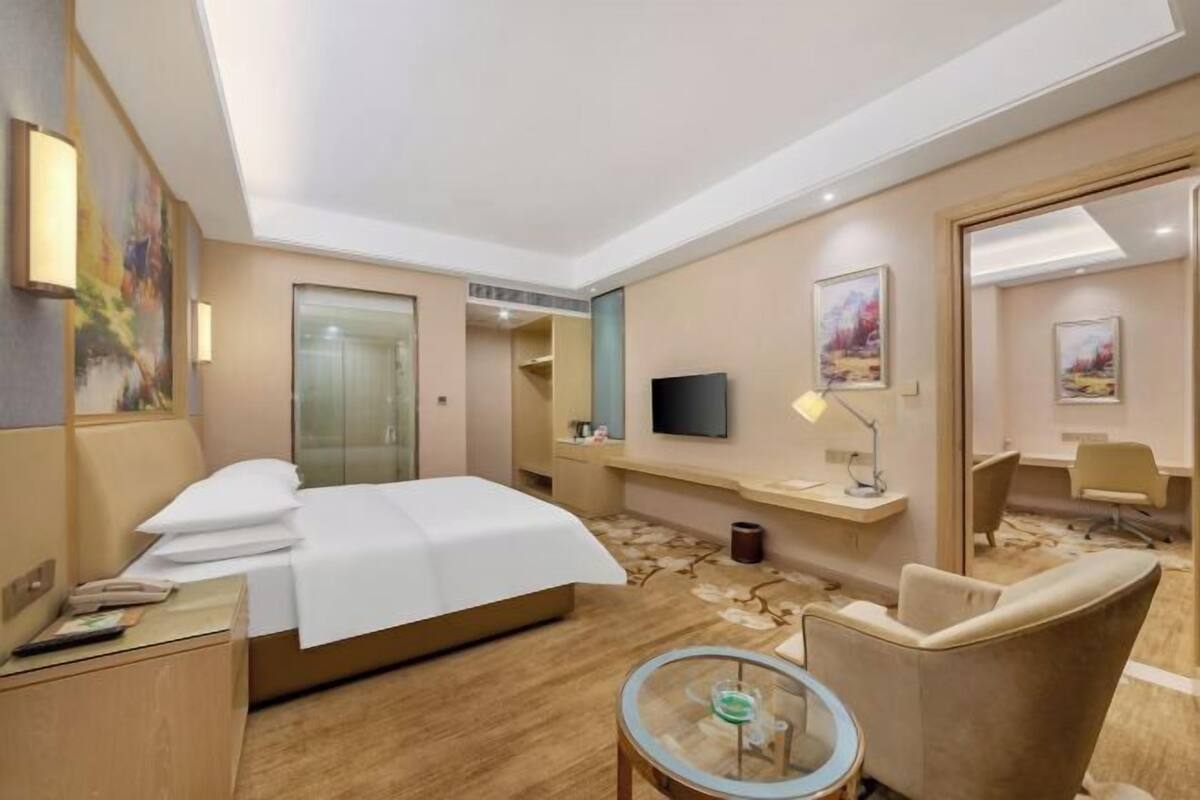 A hotel room with a bed, bedside table, lamp, chair, TV, and artwork on the walls.