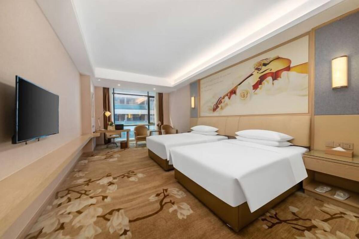 A hotel room with two beds, a flat-screen TV, a desk with a chair, and a large window.
