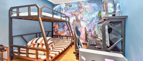 Una cama litera con escritorio y equipo de cómputo, un mural colorido en la pared y una botella de agua sobre el escritorio.