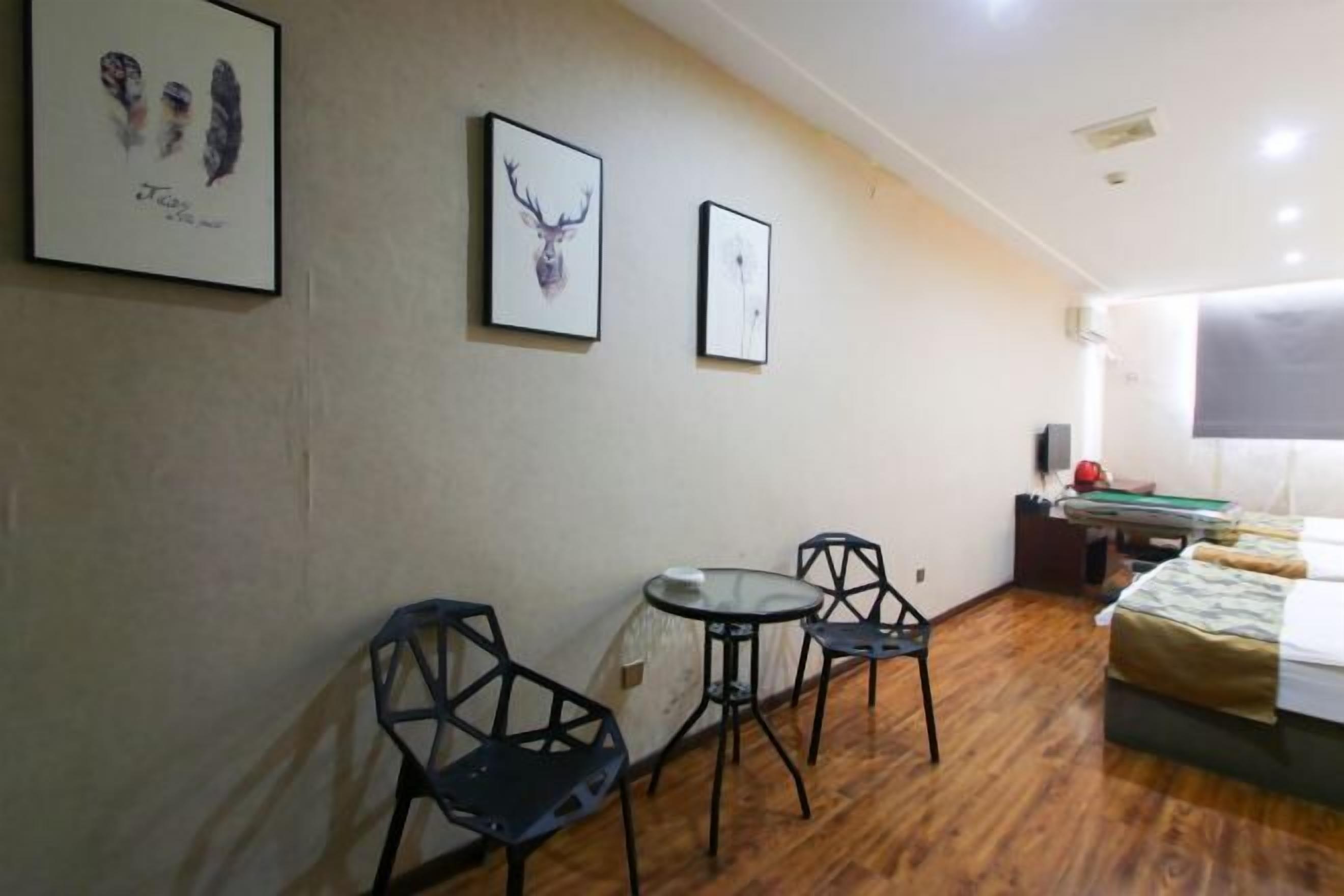 A room with a bed, a small round table, two chairs, and two framed pictures on the wall.