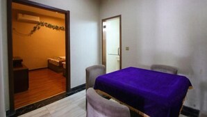 A room with a dining table covered with a purple tablecloth, two chairs, a wooden floor, and a doorway leading to another room with a bed and a small table. - Zichen Express Hotel (Santajizhen People's Government Branch) (Fuyang)