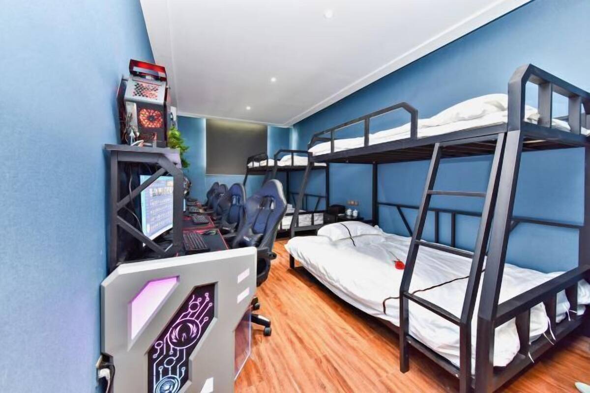 Une chambre avec un lit superposé, un bureau et une chaise, un ordinateur et une console de jeux.