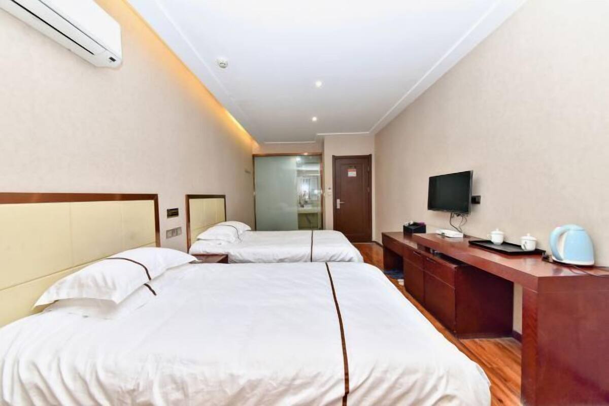 Une chambre d’hôtel avec deux lits, un bureau doté d’une télévision à écran plat, une bouilloire et un appareil de climatisation.
