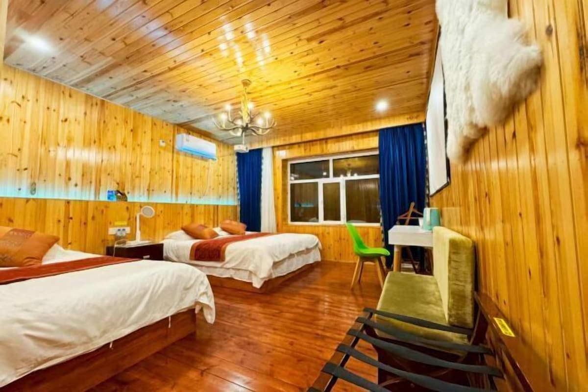 A wooden-paneled room with two beds, a desk, and a chair.