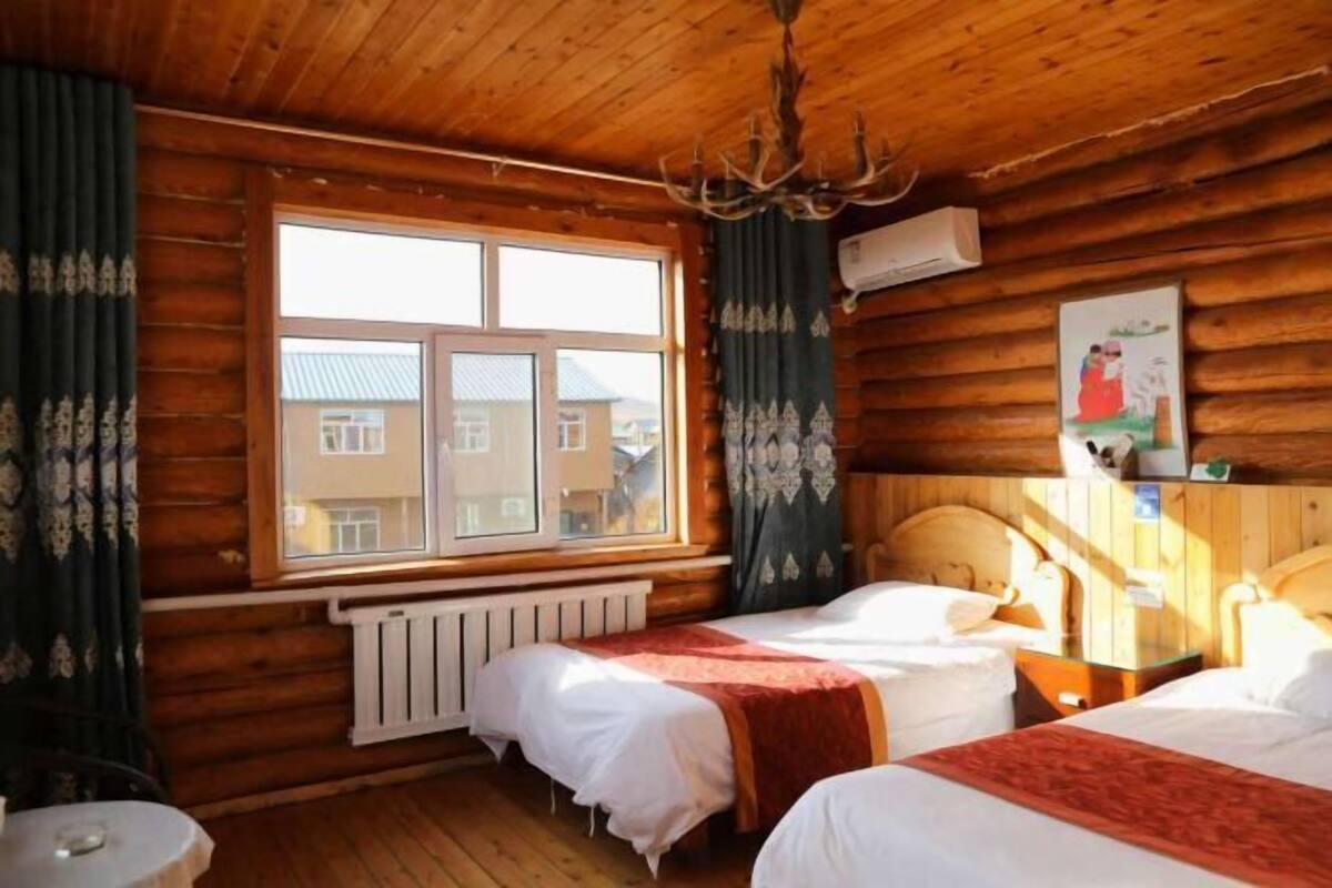 A log cabin room with two beds, a window, a radiator, and a wooden ceiling.
