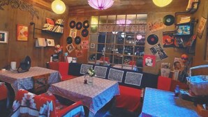 A cozy restaurant with wooden walls, vinyl records, and red seating. Tables are covered with patterned tablecloths. - September Huizhou Inn (She County)