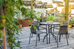 Un patio exterior con una mesa redonda y cuatro sillas, rodeado de plantas en macetas y una terraza de madera.