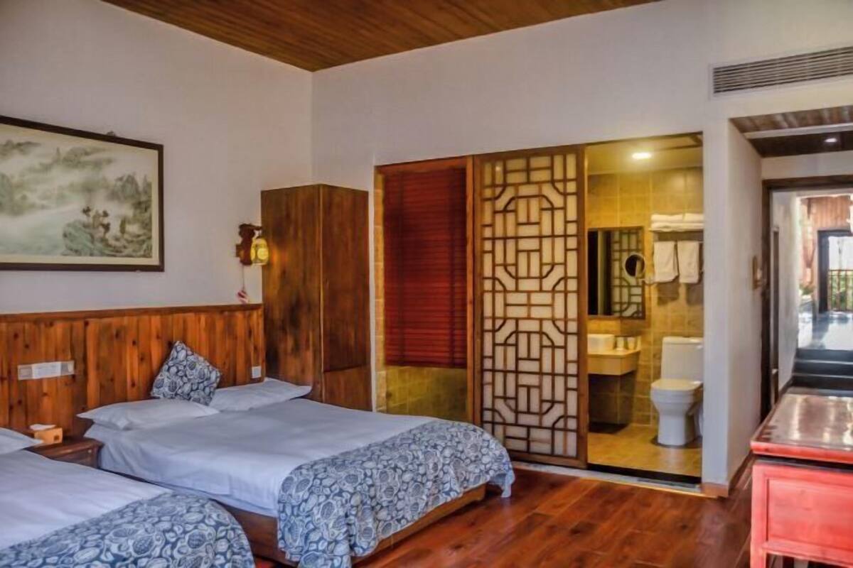 A room with two beds, a wooden headboard, a painting, a sliding door to a bathroom, and a red cabinet.