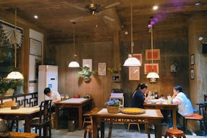 Interior de restaurant amb taules i cadires de fusta, llums penjants i un ventilador al sostre.