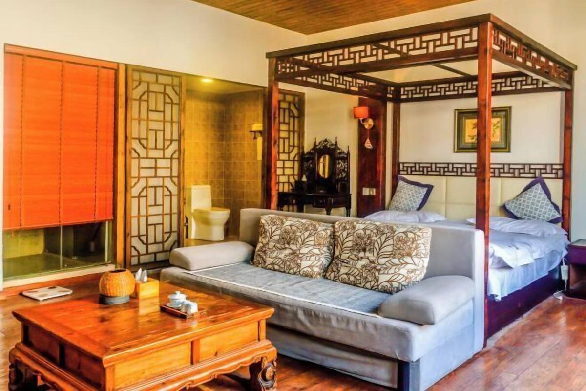 A traditional room with a four-poster bed, a sofa, a wooden coffee table, and a sliding door.