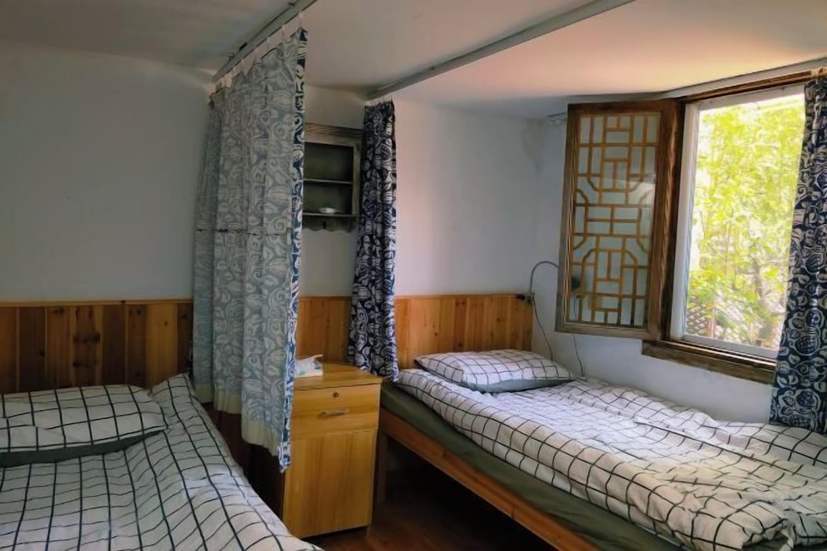 Habitació amb dos llits, un taulell de fusta, una finestra amb vista i una cortina.