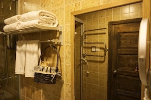 Un bany amb dutxa, una barra de tovalloles, una porta de fusta i un prestatge per a tovalloles.