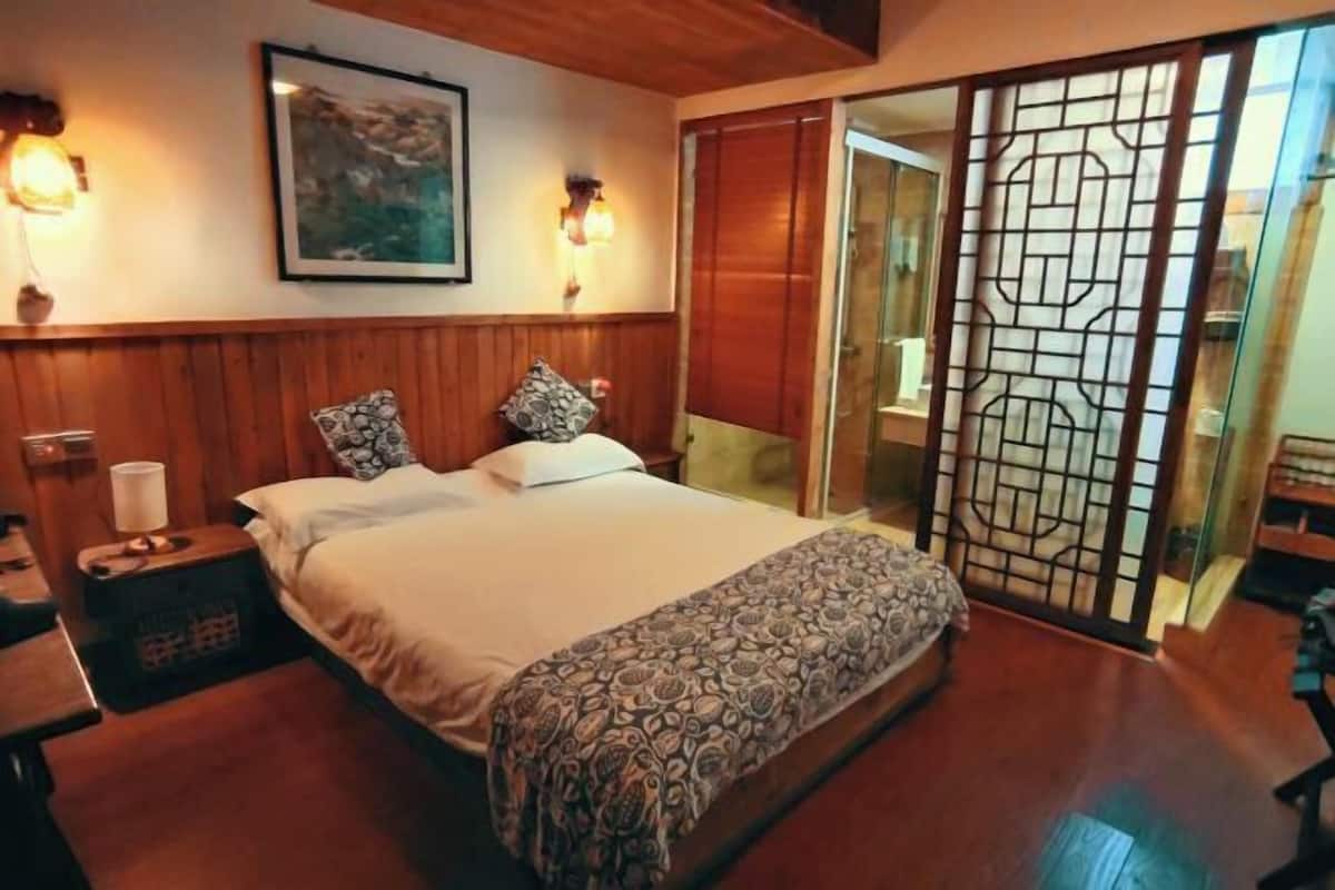 A bedroom with a bed, bedside tables, a wall-mounted lamp, a framed picture, and a sliding door with a decorative screen.