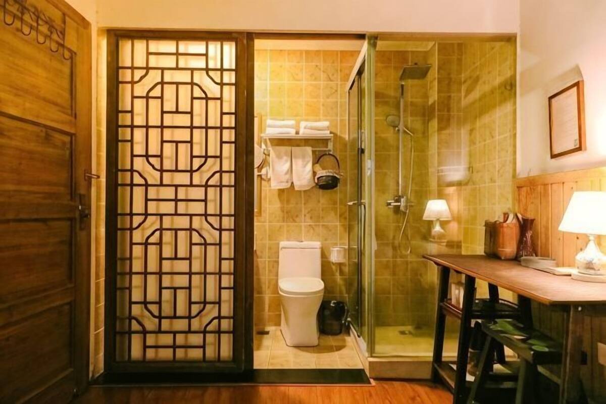 A bathroom with a toilet, shower, and a table with a lamp.