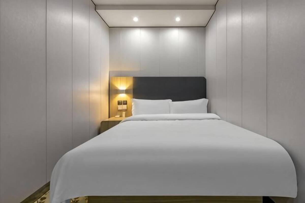 A neatly made bed with a headboard, a bedside lamp, and a wall-mounted light fixture.