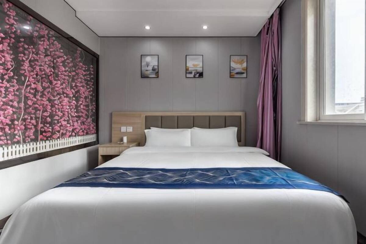 A hotel room with a bed, nightstand, and wall art.