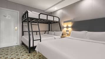 Una habitación de hotel con literas, una mesita de noche con lámpara y un suelo estampado.