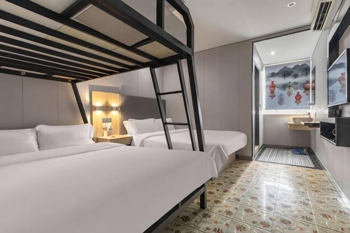 A hotel room with bunk beds, a desk, a TV, and a window with a view.