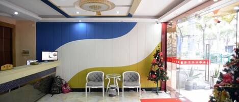 A hotel reception area with a reception desk, two chairs, a small table, a Christmas tree, and a red carpet.