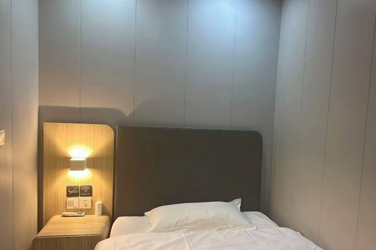 A hotel room with a bed, a nightstand with a lamp, and a wall-mounted control panel.