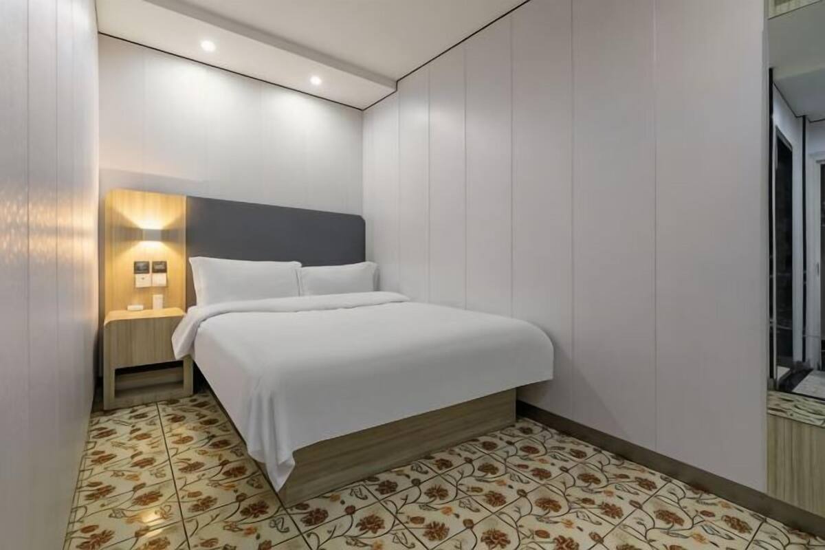 A neatly arranged hotel room with a bed, bedside table, and a wall-mounted light fixture.