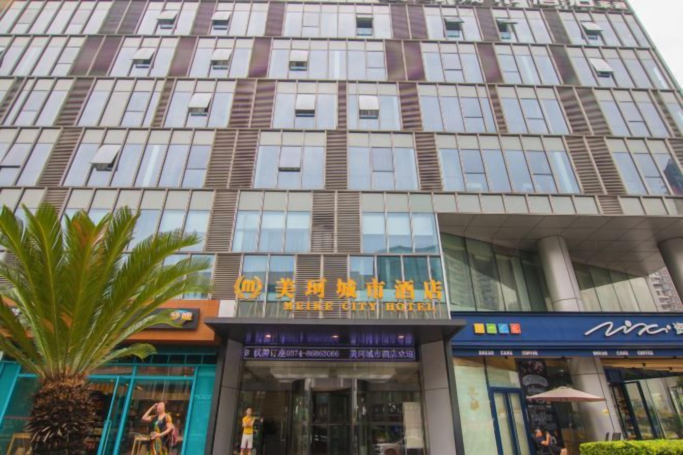 A modern building with a glass facade, a palm tree in front, and a sign for a hotel.