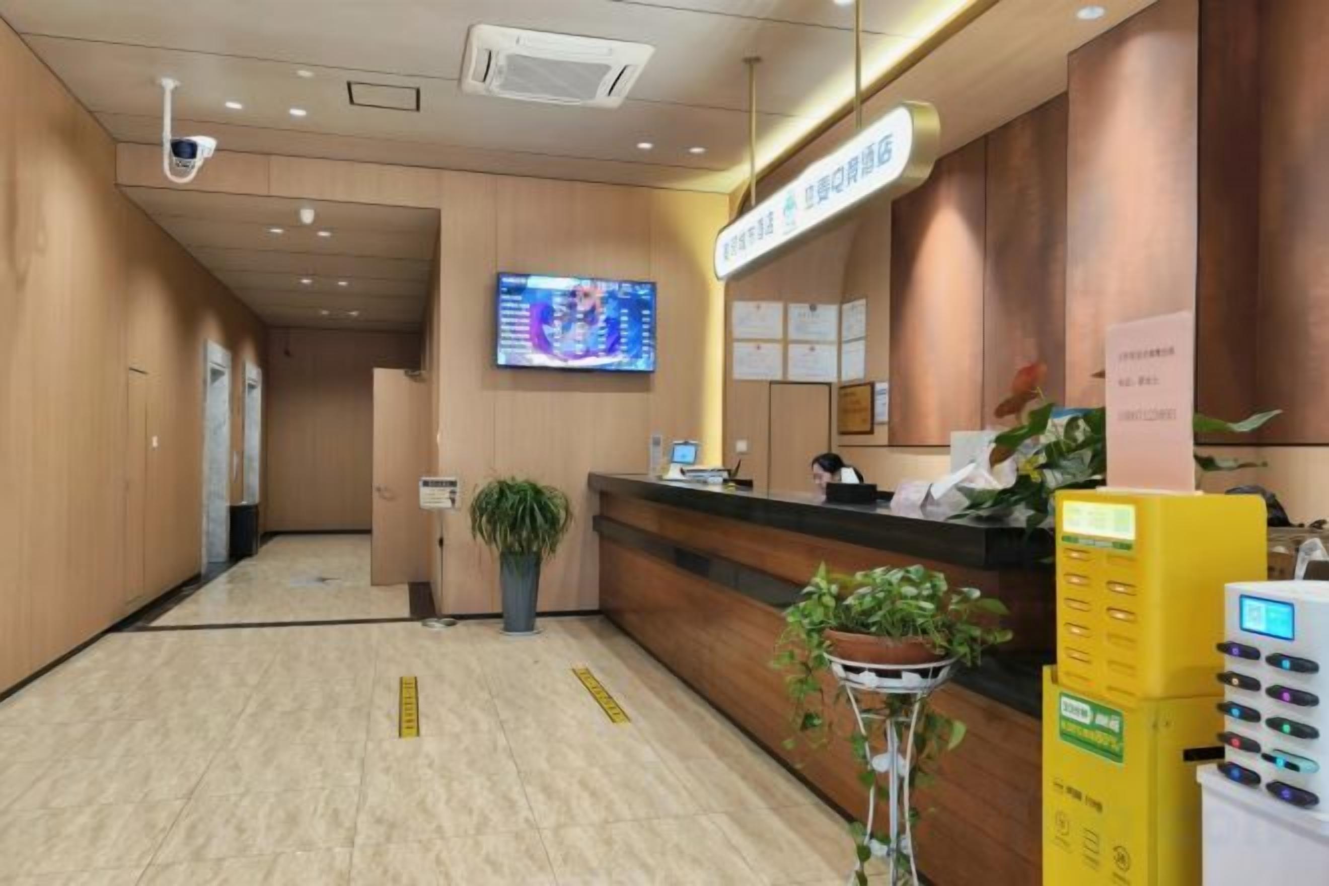 A hotel reception area with a reception desk, a digital screen, and a plant.