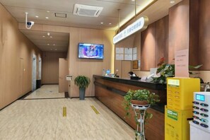 Zona de recepción de un hotel, con mostrador de recepción, pantalla digital y una planta.