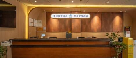 A hotel reception area with a reception desk, a sign indicating the hotel's name, and a plant to the right.