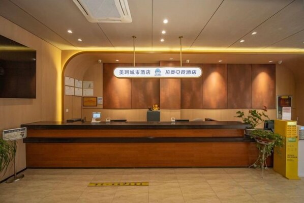 A hotel reception area with a reception desk, a sign indicating the hotel's name, and a plant to the right.