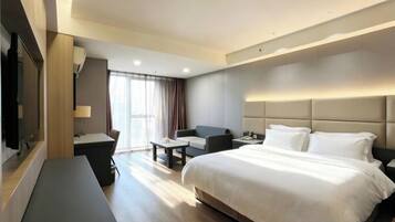 Una habitación de hotel con cama, escritorio, silla, televisor y ventana con cortinas.