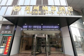 Entrada de un hotel con puerta giratoria, fachada de vidrio y señalización en idioma extranjero.