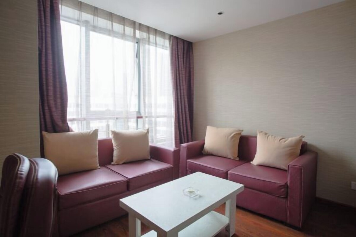 A room with two sofas, a small white table, and a window with sheer curtains.