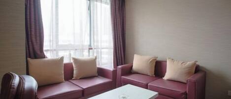 A room with two sofas, a small white table, and a window with sheer curtains.