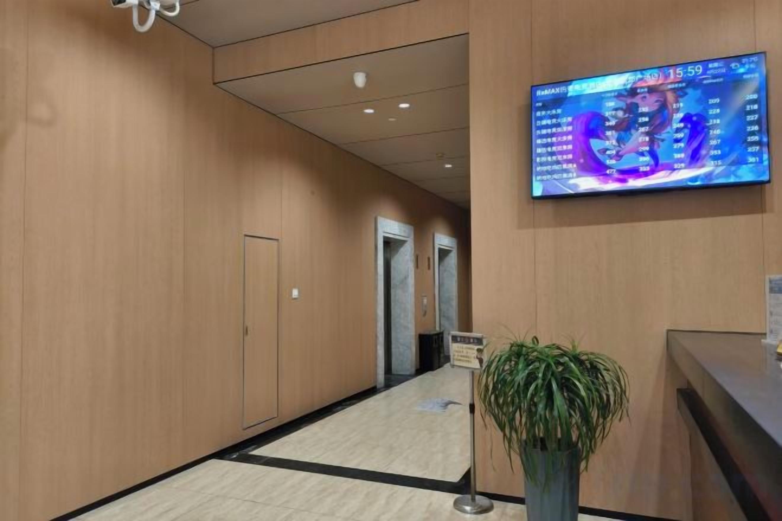 A hotel reception area with a digital display, a reception desk, and a plant.
