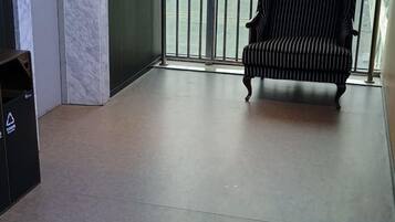 A room with a tiled floor, a trash bin, a chair, and a glass door leading to an outdoor area.