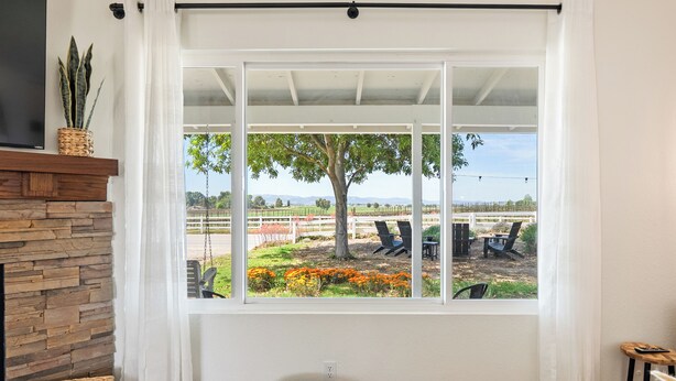 A room with a large window, a stone wall, a wooden floor, a grey pouf, and a wicker basket. - Boots & Barrels Ranch-2 master bedrooms,2 add'l bedrooms,3 baths, views, firepit (Paso Robles)