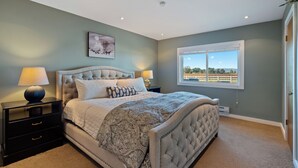 A bedroom with a large bed, two bedside tables, a nightstand, a window with a view, and a ceiling light. - Boots & Barrels Ranch-2 master bedrooms,2 add'l bedrooms,3 baths, views, firepit (Paso Robles)