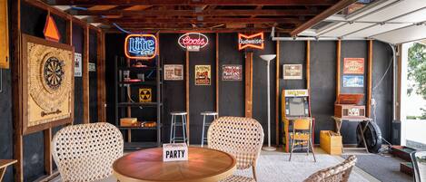 A room with a dartboard, a neon sign for Budweiser, a neon sign for Coors Light Beer, and a sign for a party.
