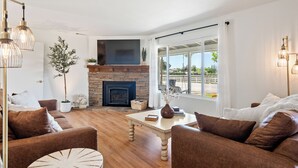 A living room with a fireplace, a large window, and a view of the outdoors. - Boots & Barrels Ranch-2 master bedrooms,2 add'l bedrooms,3 baths, views, firepit (Paso Robles)