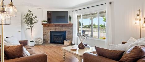 A living room with a fireplace, a large window, and a view of the outdoors.