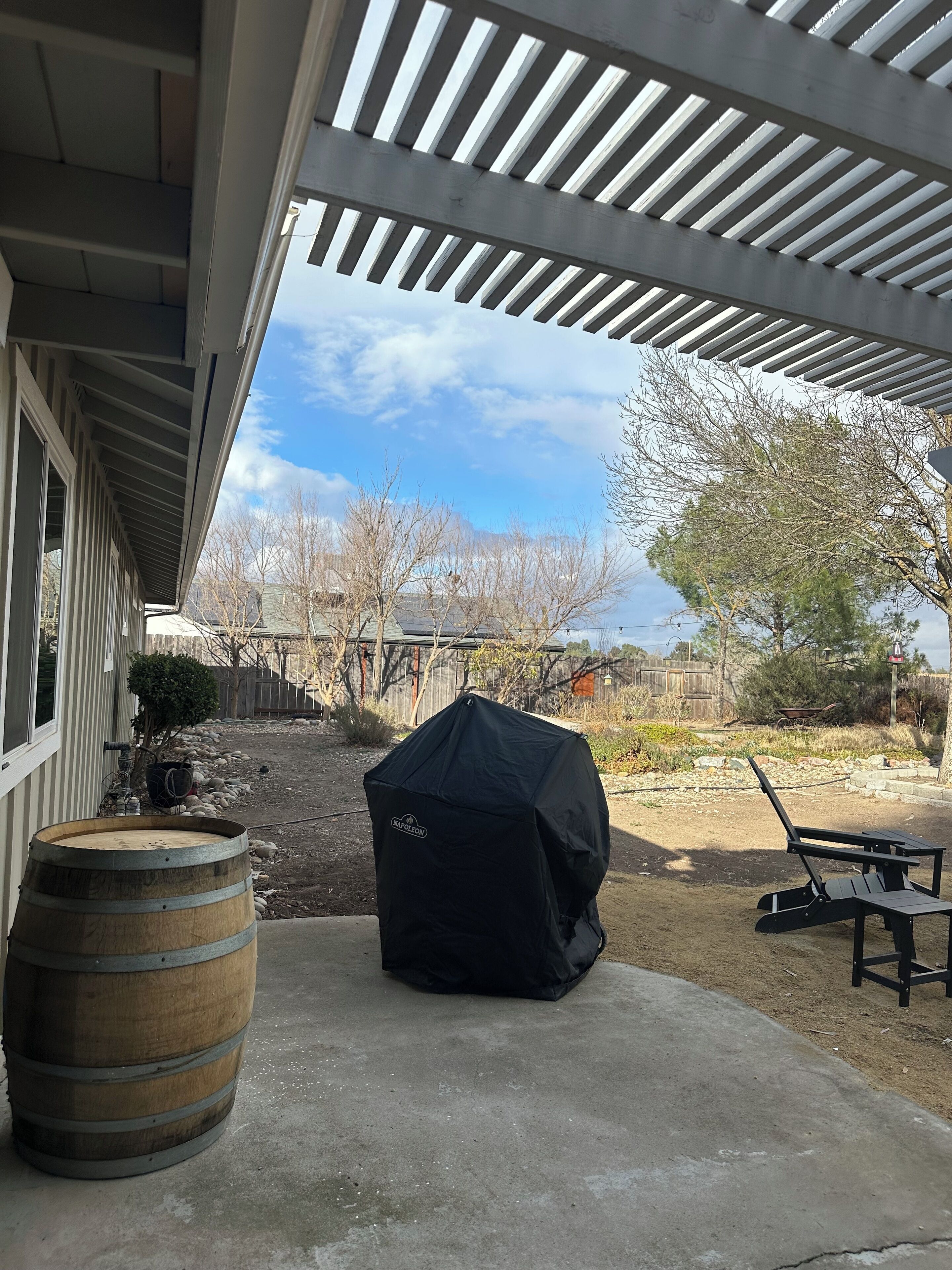 A covered patio area with a barbecue grill, a wooden barrel, and a picnic table.