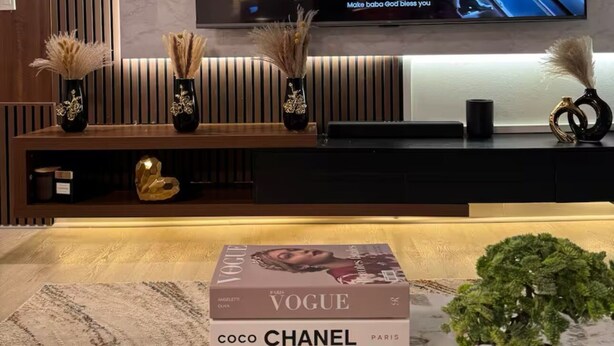 Un salon moderne avec un grand téléviseur à écran plat fixé au mur, un meuble de rangement en bois en dessous et une plante en pot posée sur le sol.