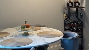 Un coin repas avec une table ronde, des chaises recouvertes d’un tissu bleu, un meuble à vin et des vases décoratifs.