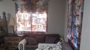 A living room with a sofa, a lamp, and a window with a view of buildings. - Cozy 1-bedroom house in beautiful Orlando with AC (Orlando)