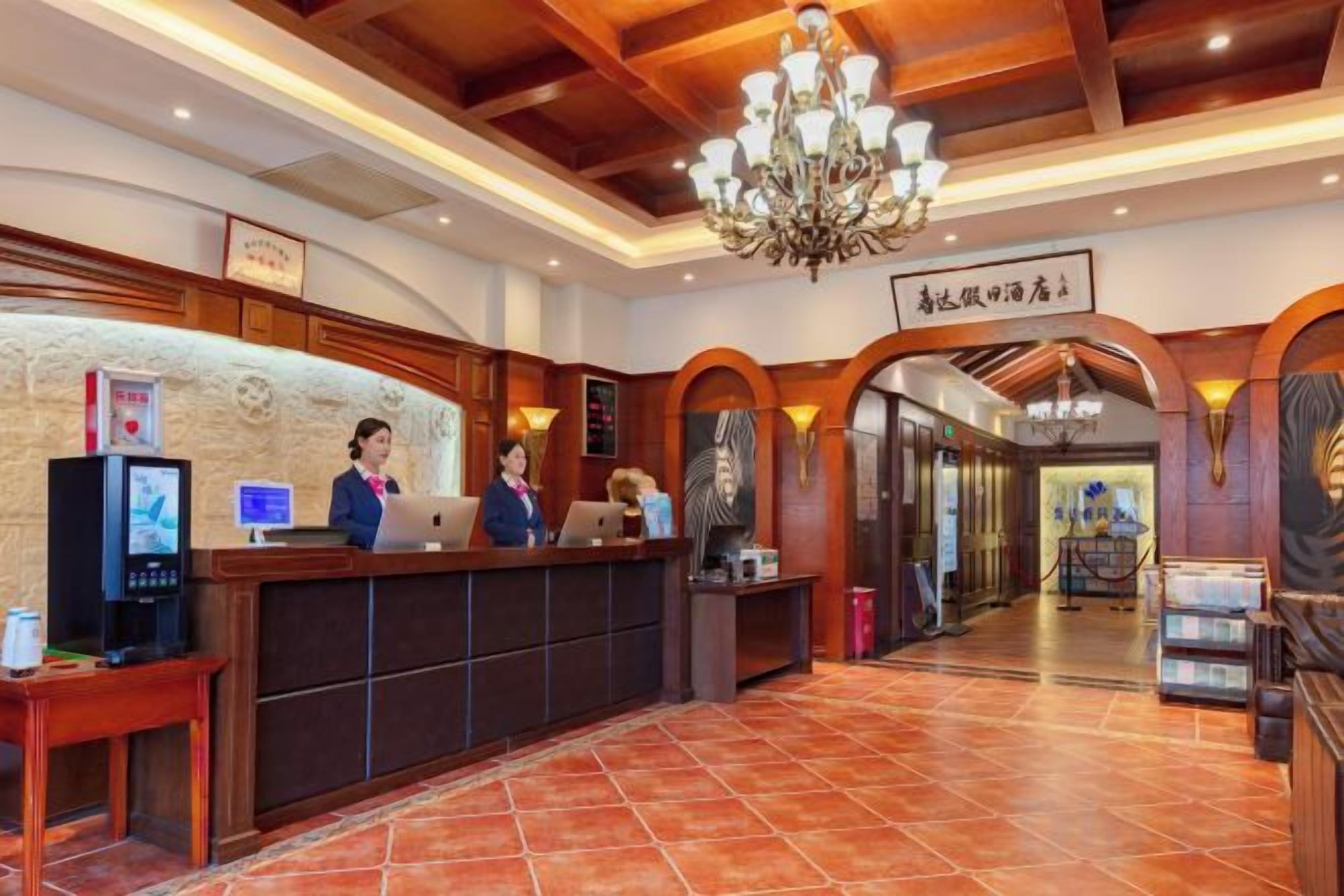 Un hall d'hôtel comprenant un comptoir d'accueil, du personnel, un lustre et une enseigne indiquant le nom de l'hôtel.
