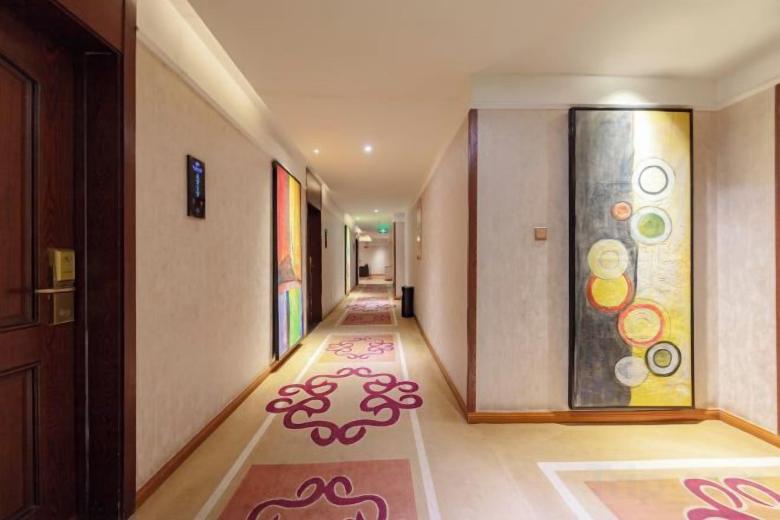 A hotel corridor with a carpeted floor, a door on the left, and a wall with a circular pattern.