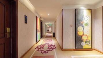 Pasillo de hotel con piso alfombrado, una puerta a la izquierda y un muro con diseño circular.